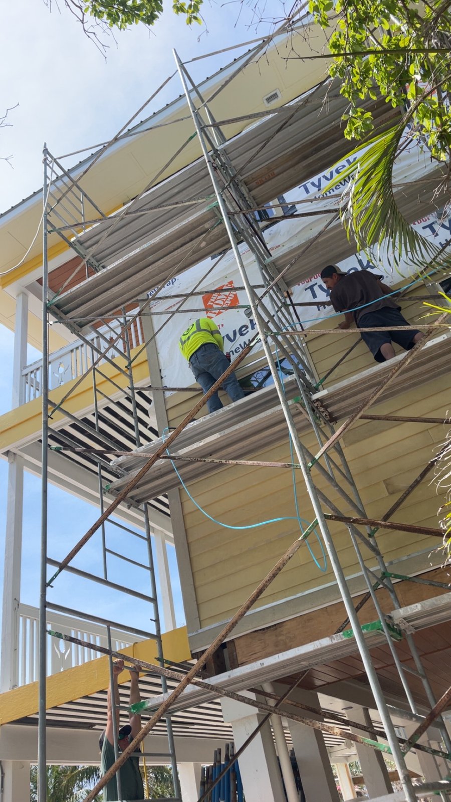 Crew installing yellow lap siding and house wrap on elevated home with scaffolding