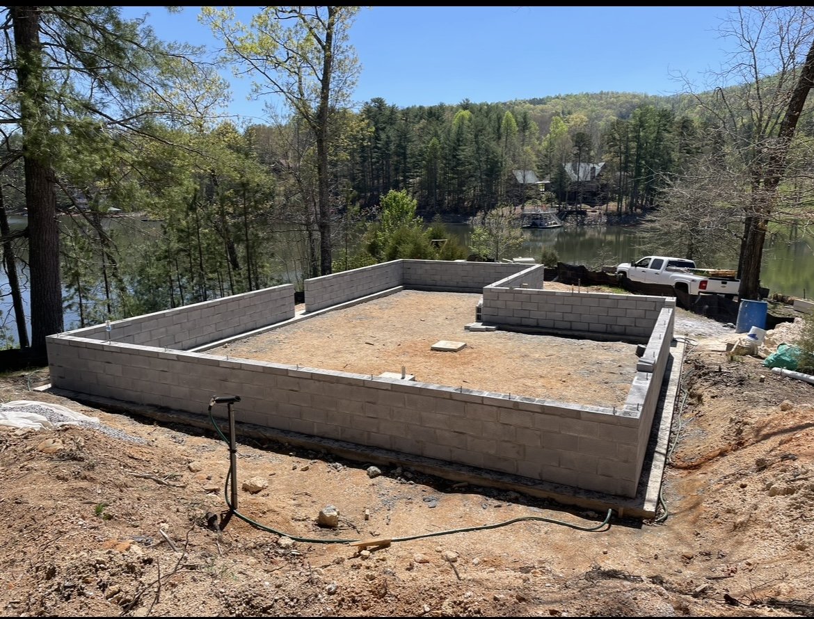 Concrete block foundation on a sloped lakeside lot with truck and materials nearby