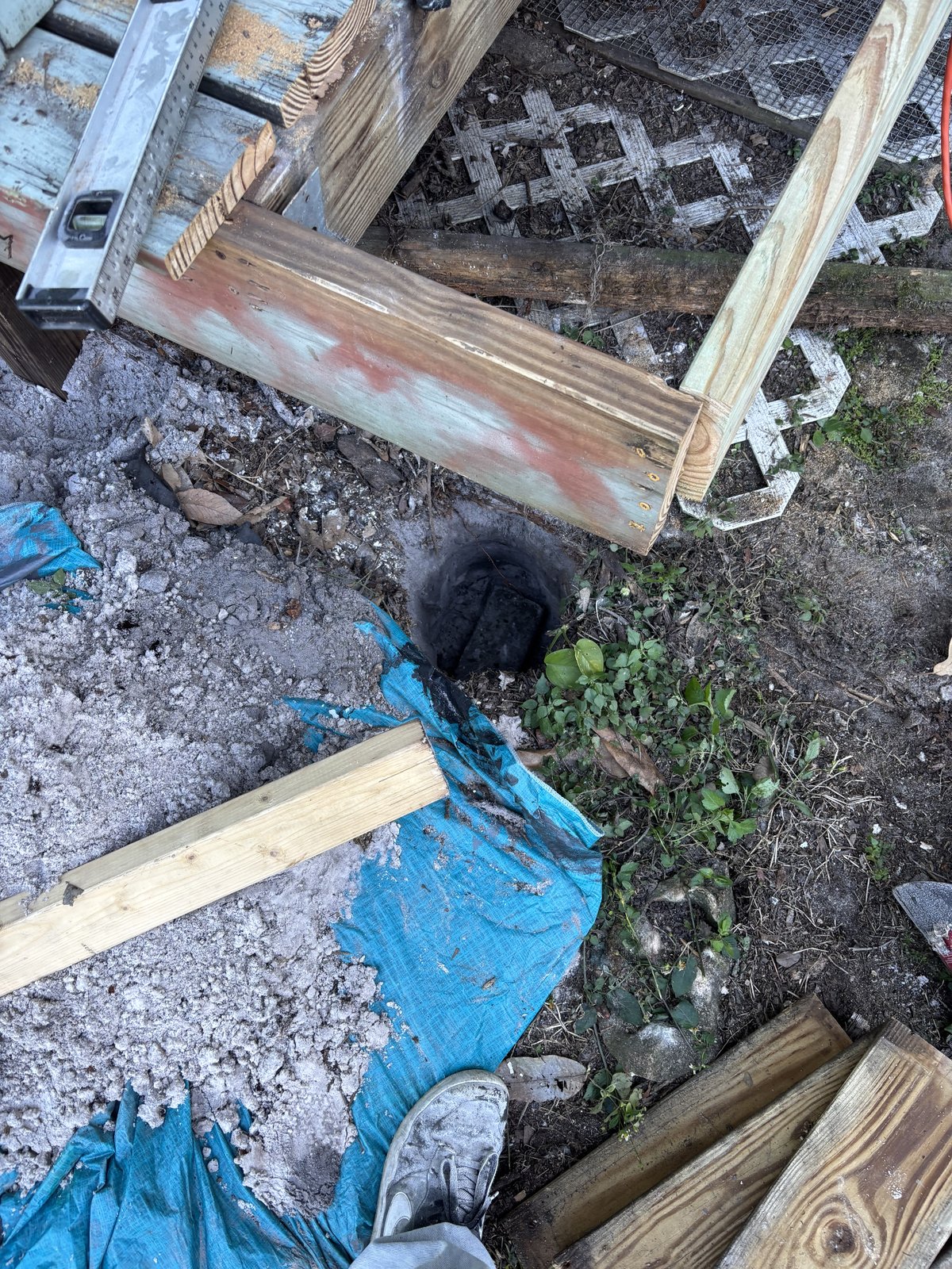 Deck repair site with excavated footer hole, lumber, and spirit level on framing