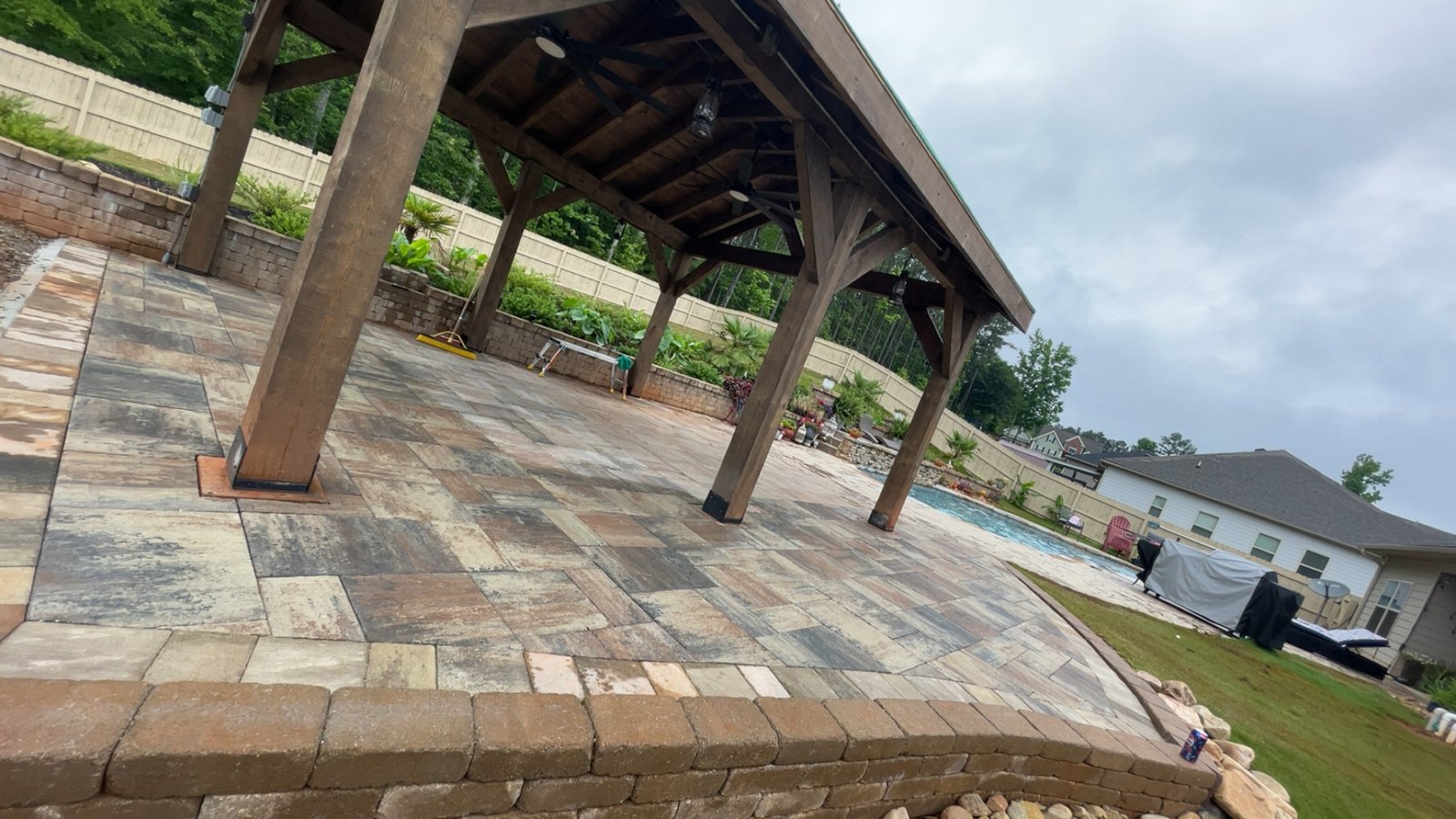Finished wooden pavilion over multi-tone stone paver patio next to a backyard pool
